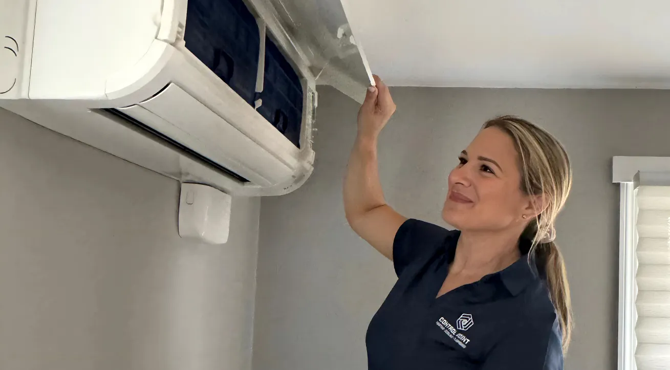 Female technician in a navy blue uniform inspecting or cleaning a wall-mounted air conditioning unit.