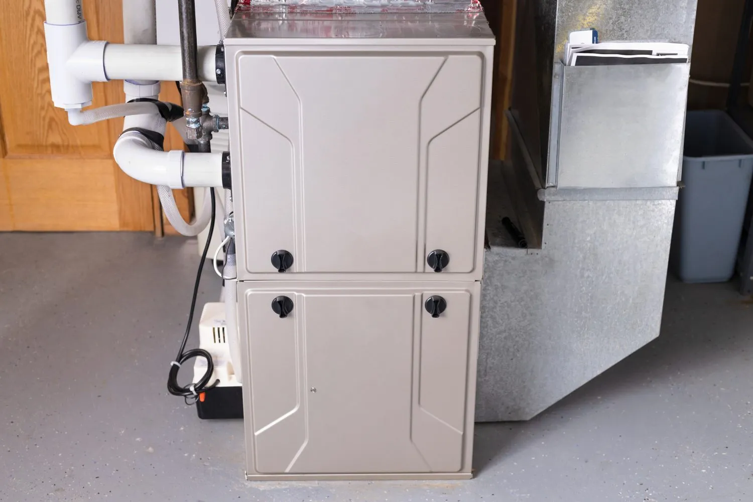 High-efficiency residential furnace with PVC pipes and ductwork installed in a basement utility room.