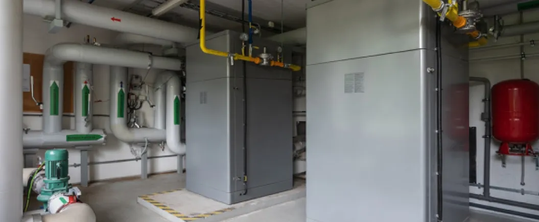 Industrial heating system with large boilers, pipes, and valves in a mechanical room.